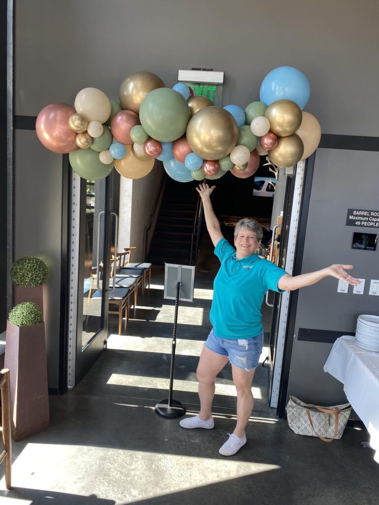 Dorothy of Festive Balloons standing next to a custom Freeform Garland balloon decor